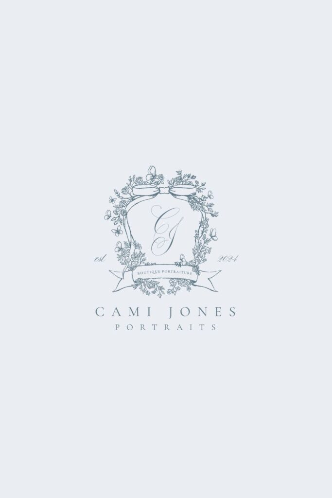Close-up of the Cami Jones Portraits crest logo with intricate floral details, butterfly accents, and a ribbon banner reading “Boutique Portraiture.”