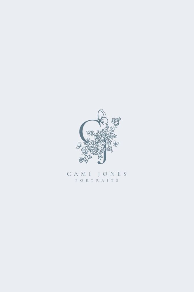 Close-up of the Cami Jones Portraits crest logo with intricate floral details, butterfly accents, and a ribbon banner reading “Boutique Portraiture.”